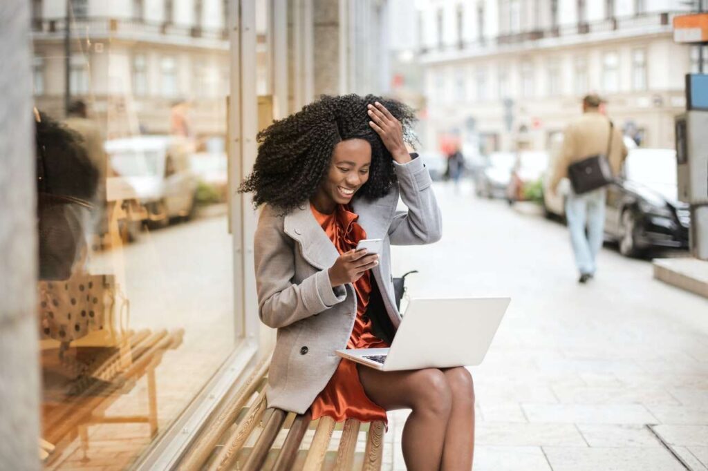 a traveler sitting on a city street, holding a laptop and looking at the screen